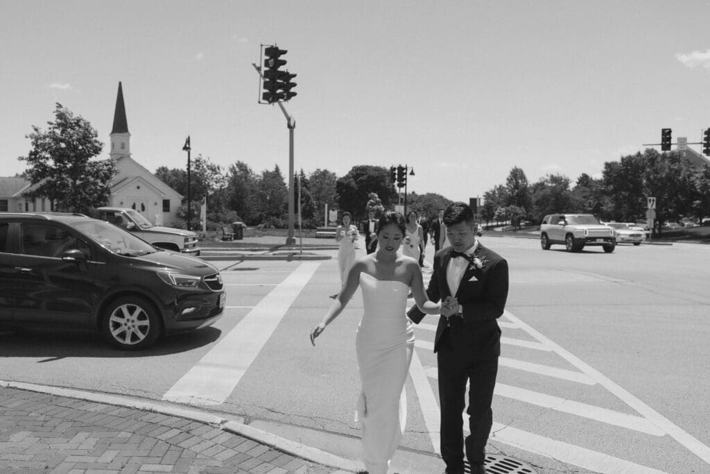 Asian bride and groom crossing the street in black and white photo.