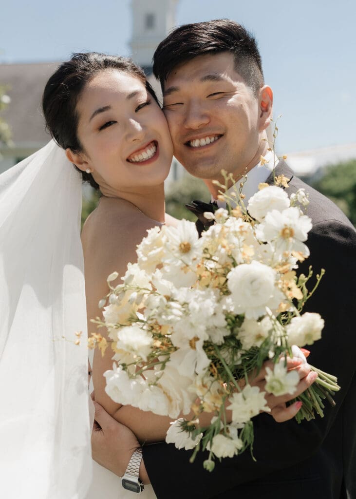 Asian bride and groom holding a bouquet posing for the camera.