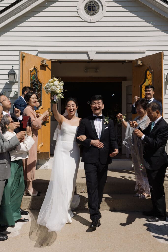 Asian bride and groom walking out of the church looking happy with a crowd clapping.