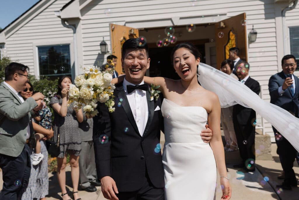 Asian bride and groom walking out of the church looking happy with a crowd clapping.