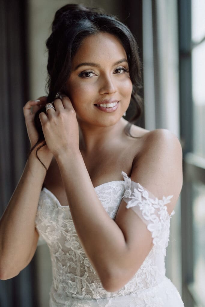Bride wearing off shoulder wedding gown putting on an earring.