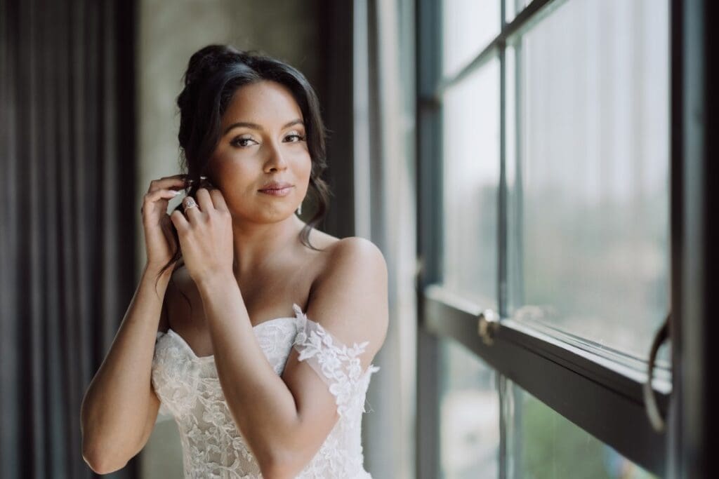 Bride wearing off shoulder wedding gown putting on an earring.