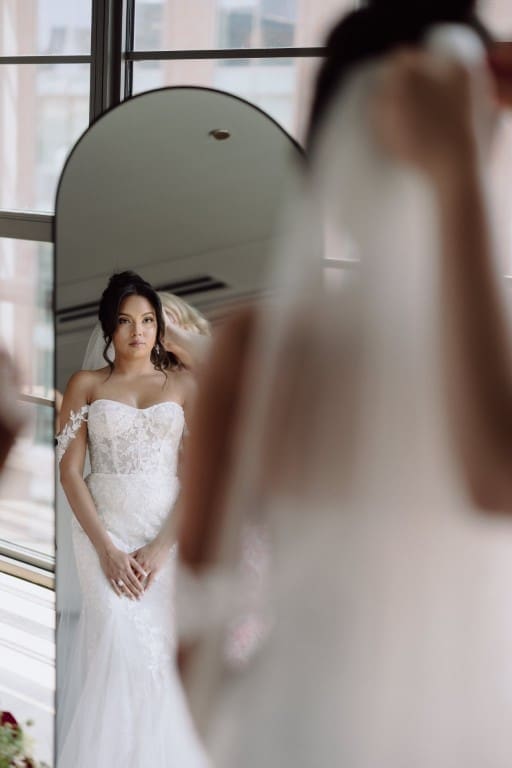 Bride wearing off shoulder wedding gown facing a mirror.