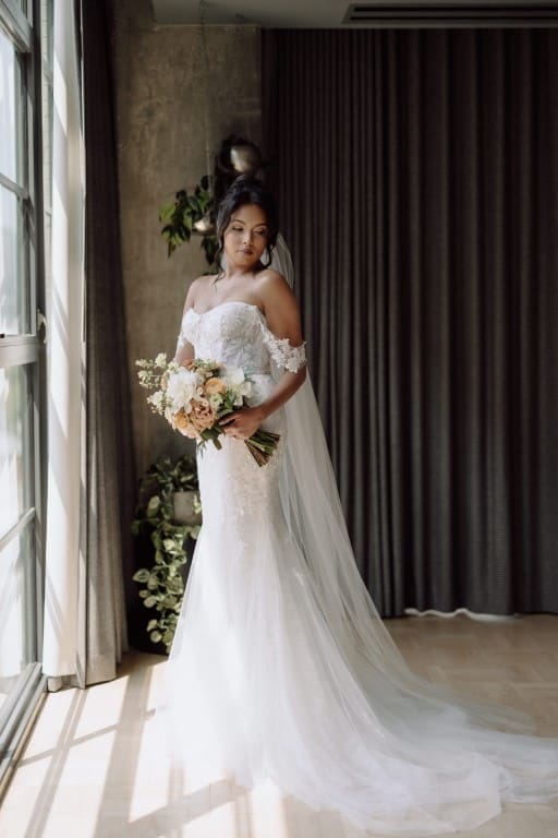 Bride wearing off shoulder wedding gown holding a bouquet.