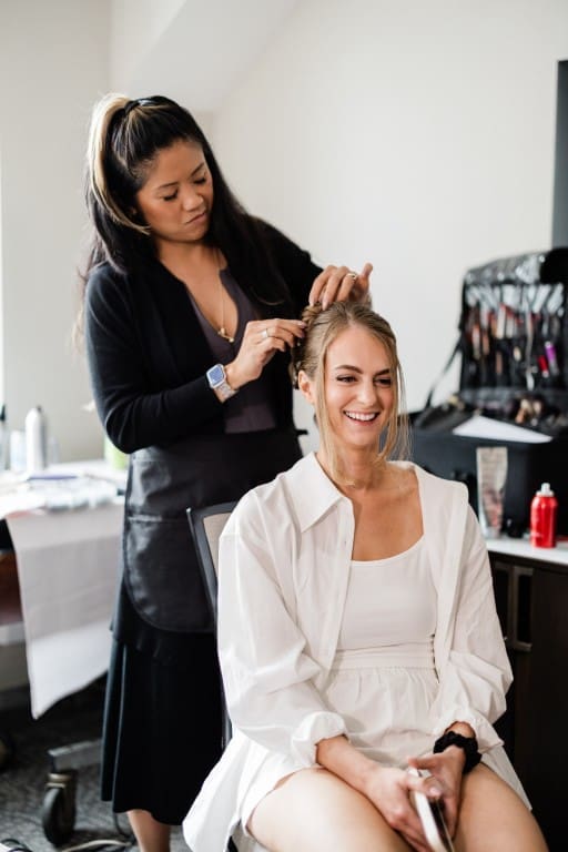 Bride sitting on a chair getting her hair fixed.