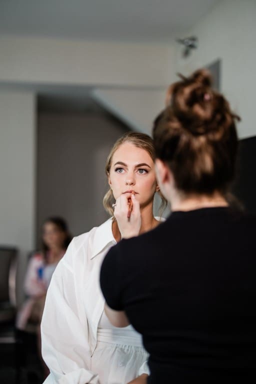 Bride sitting on a chair getting her makeup done.