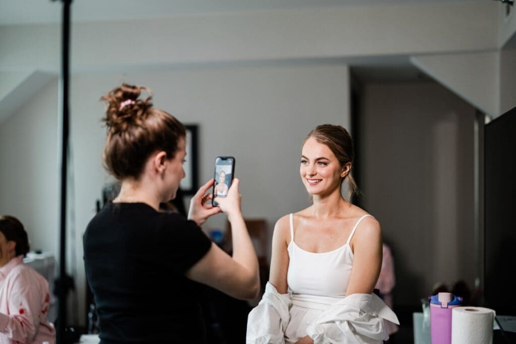 Bride posing as the makeup artist takes her picture holding a phone.