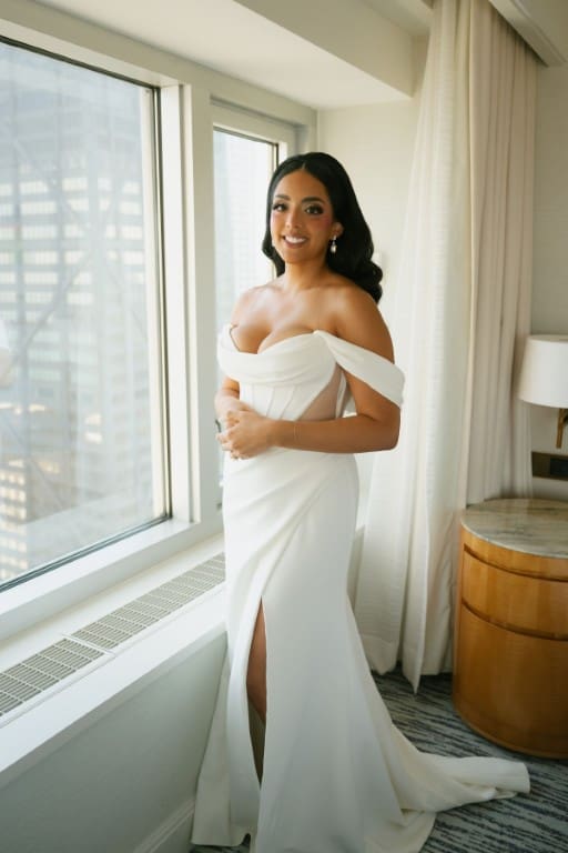 Bride smiling while standing wearing wedding gown.