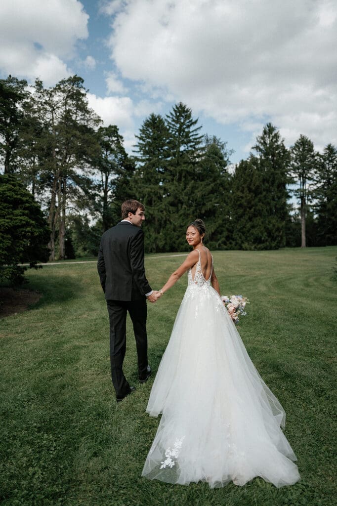 Bride and groom holding hands, walking together, smiling at each other on their wedding day.