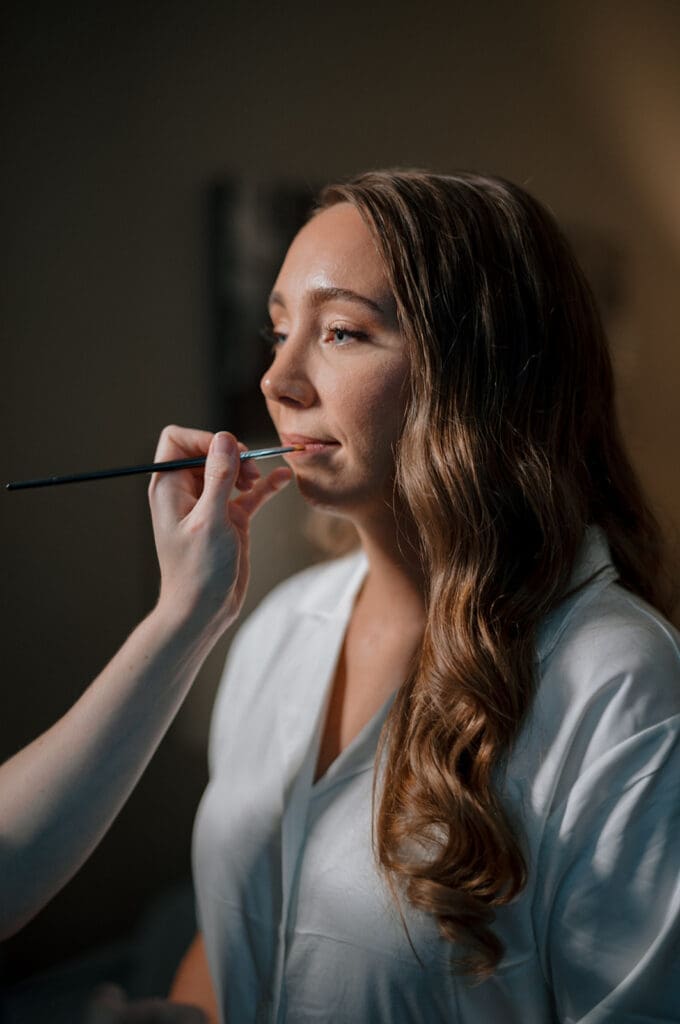 Bride with a hand putting lipstick on her lips.