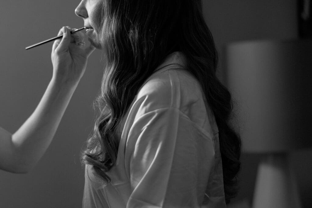 Bride with a hand putting lipstick on her lips.