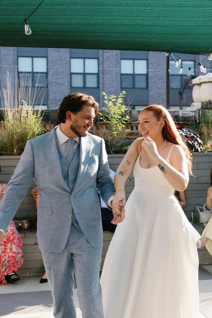 Bride and groom holding hands, smiling while walking down the aisle.