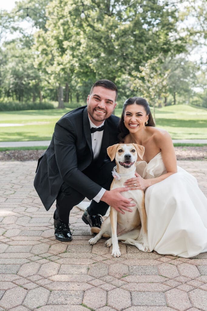Bride and groom with their dog smiling.