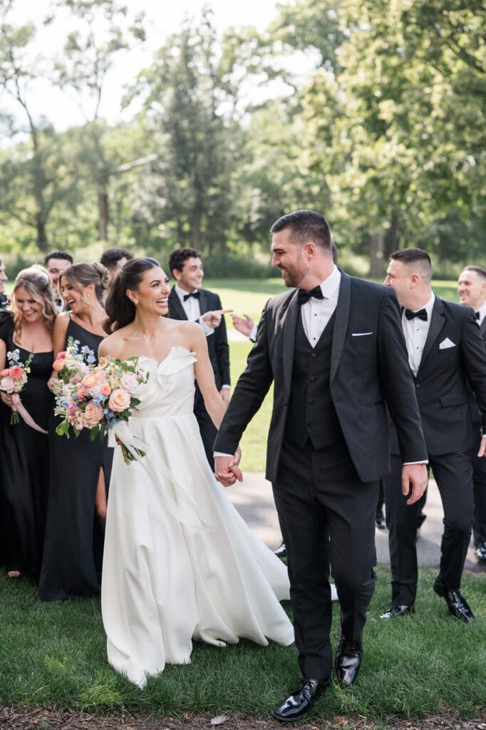 Bride and groom holding hands, walking together, smiling at each other on their wedding day.