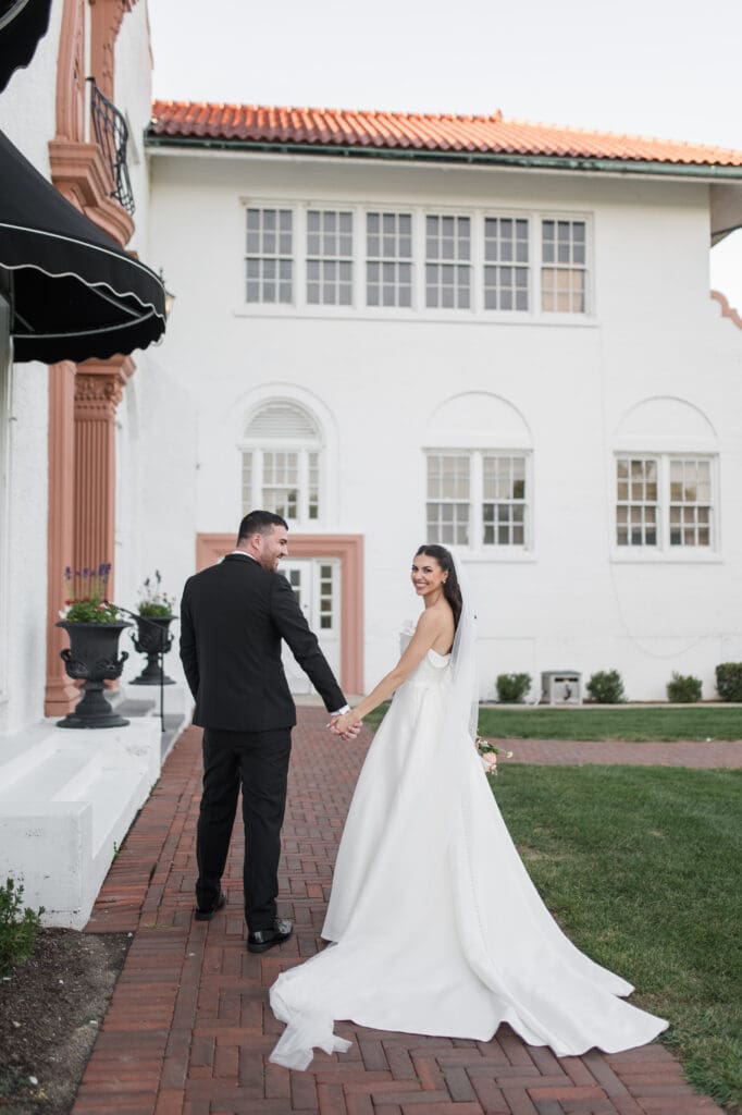 Bride and groom holding hands, walking together, smiling at each other on their wedding day.