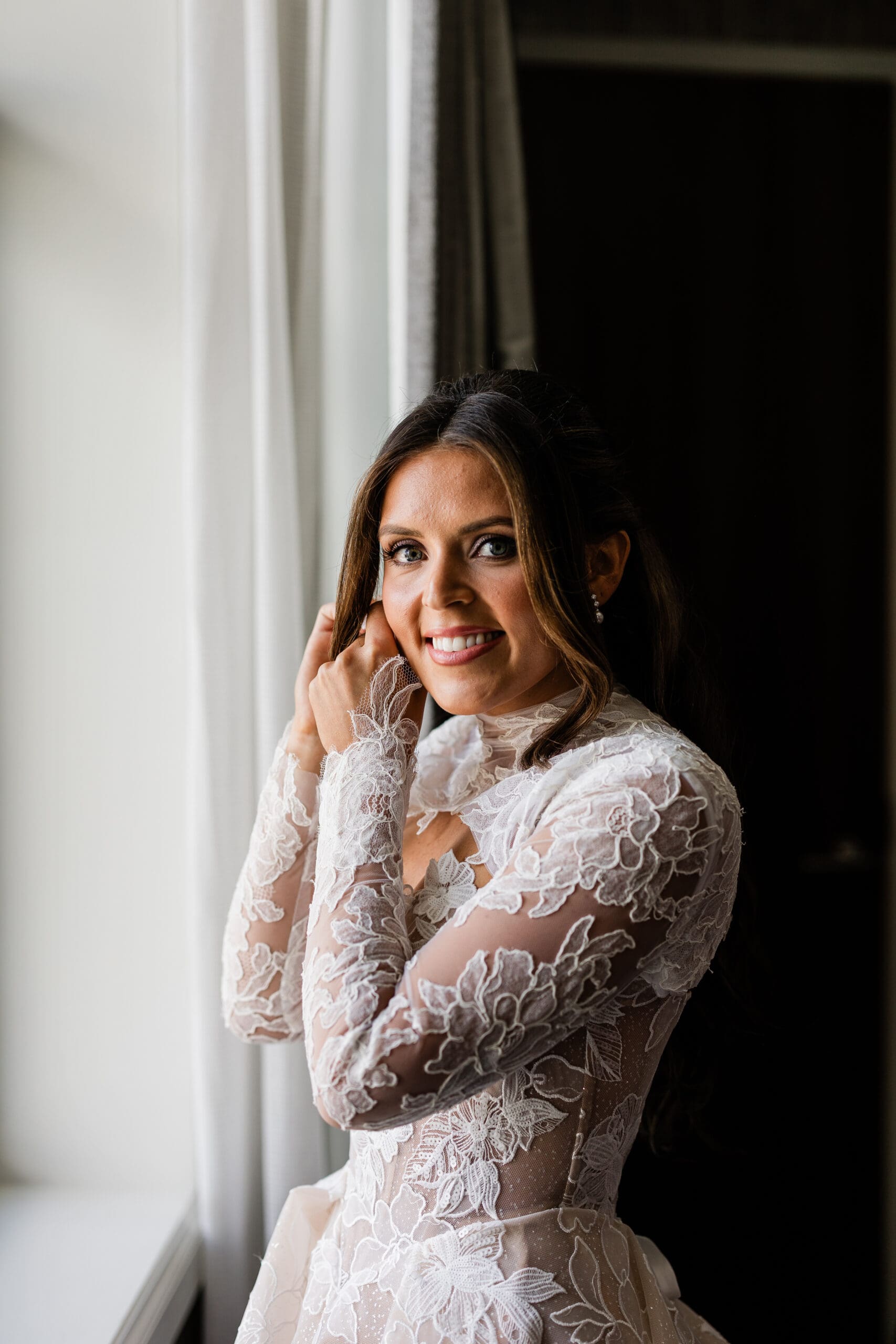 Bride holding her earring beside her face, highlighting her soft glam makeup and hairstyle.
